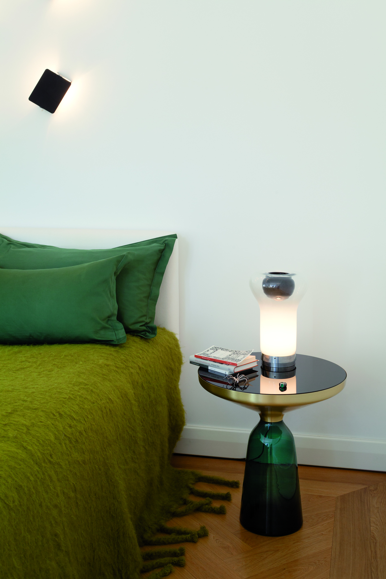 Bell Side Table Beistelltisch von ClassiCon im Schlafzimmer neben einem Bett mit grüner Tagesdecke.