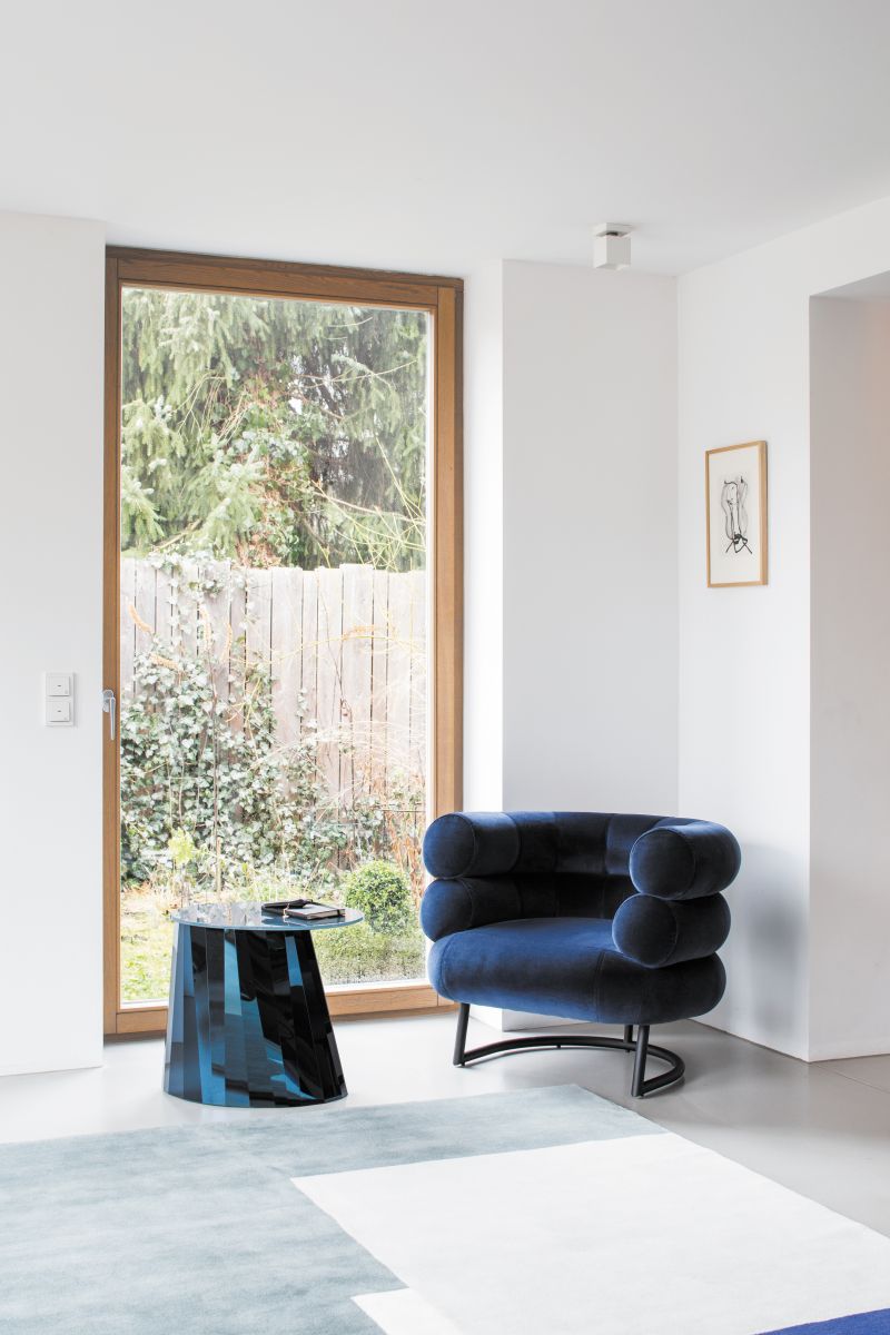 Moderner Wohnraum mit Roquebrune Teppich von ClassiCon, blauem Sessel und Beistelltisch am Fenster.