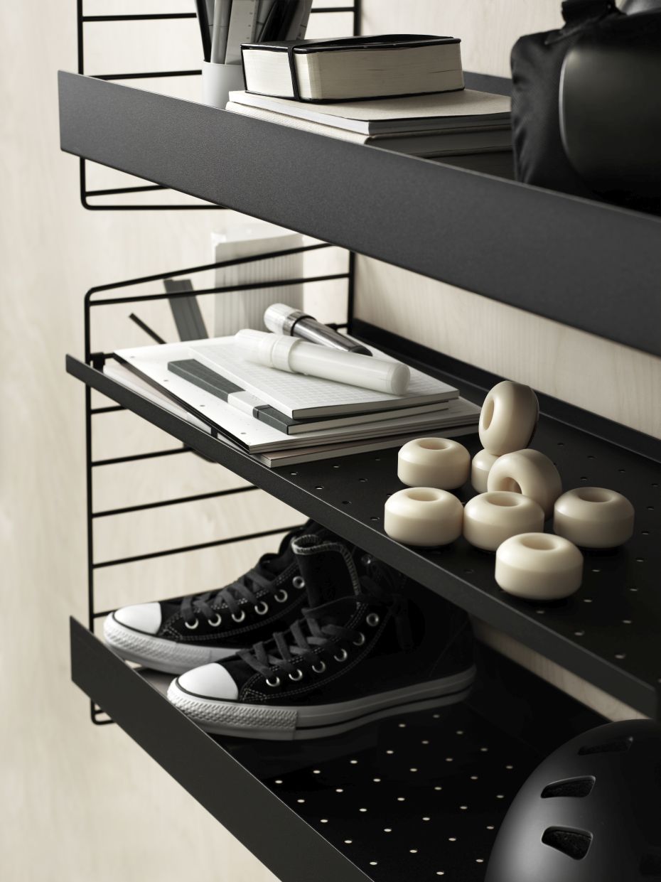 Schwarzer String Furniture Regalboden aus Metall (58cm) mit hoher Kante, beladen mit Schuhen, Rollen und Büroartikeln.