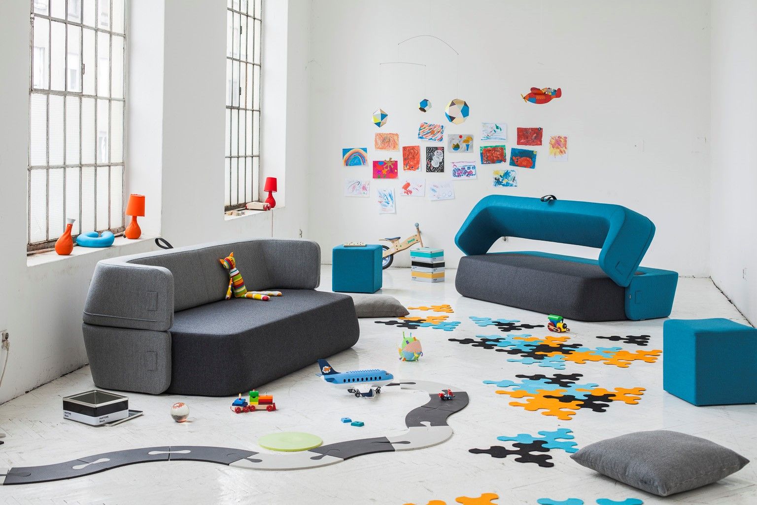 Helles Interieur mit grauem Revolve Schlafsofa von Prostoria, blauem Sessel und Spielsachen auf dem Boden.