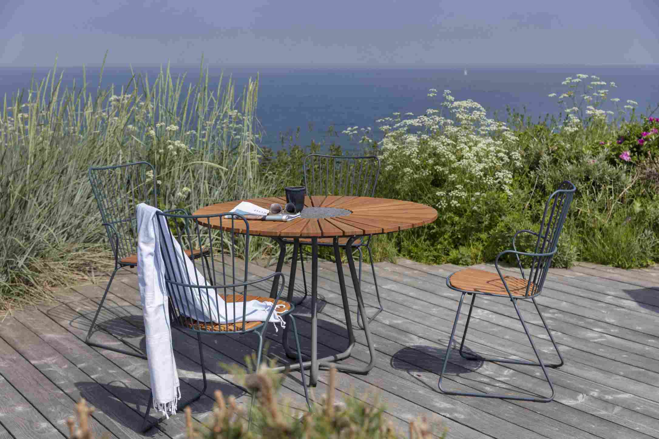 Houe Circle Outdoor Tisch Ø 110 cm mit Stühlen auf einer Holzterrasse mit Meerblick.