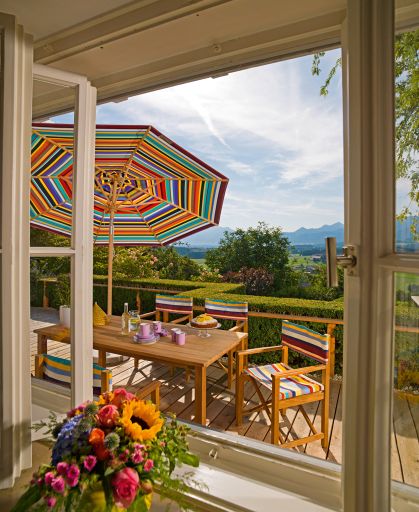 Multicolor Sonnenschirm von Weishäupl überdeckt Gartentisch und Stühle auf einer Terrasse mit Ausblick.
