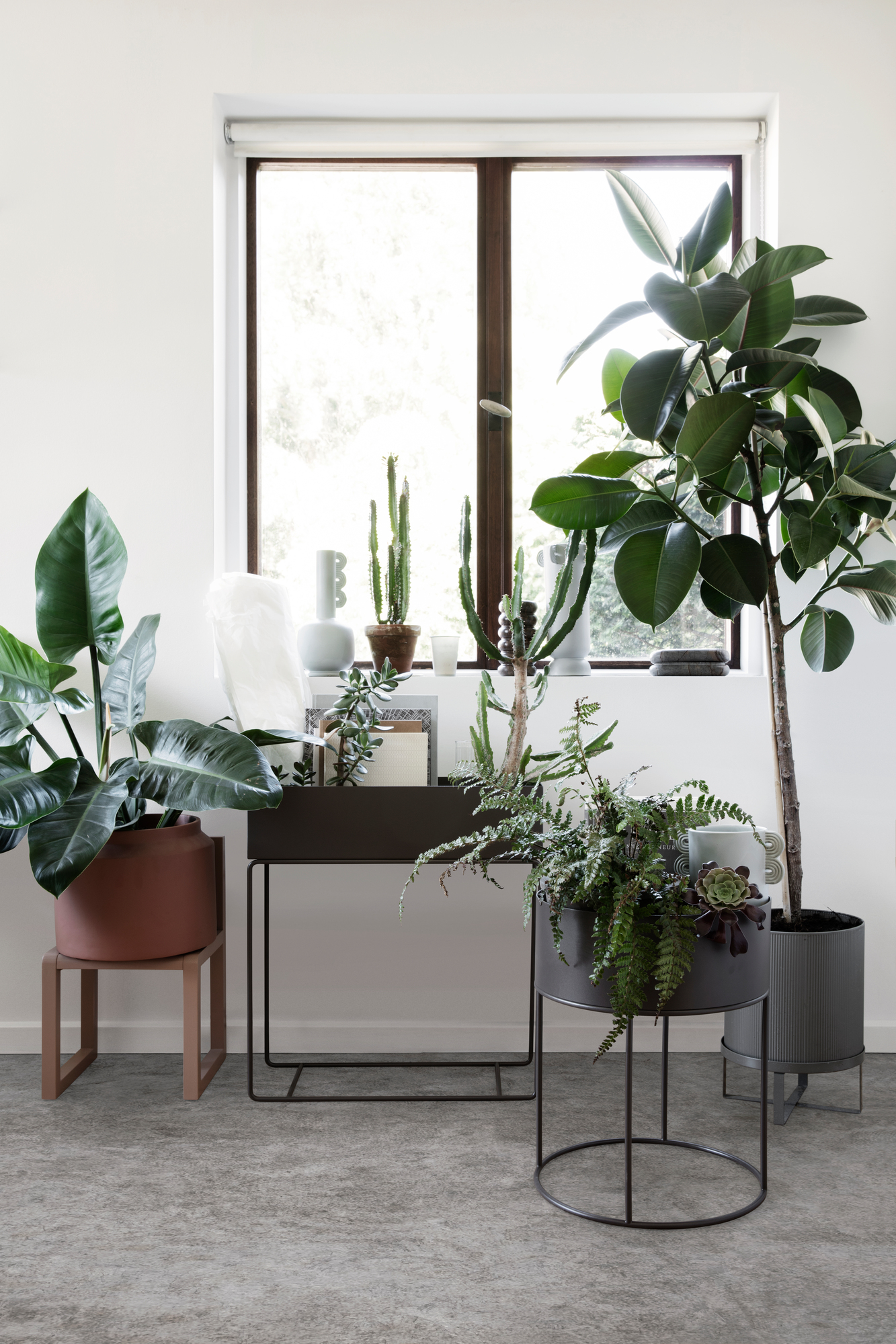 Großer, brauner Ferm Living Blumentopf mit Zimmerpflanze im modernen Wohnraum, weitere Pflanzgefäße im Hintergrund.