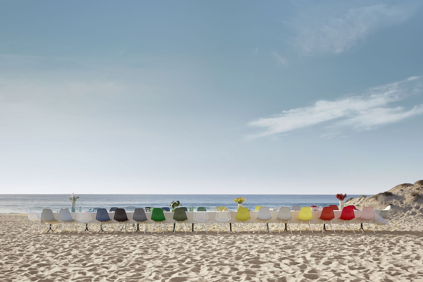 Bunte Eames Plastic Side Chairs DSX Stühle von Vitra an einem langen Tisch am Strand.