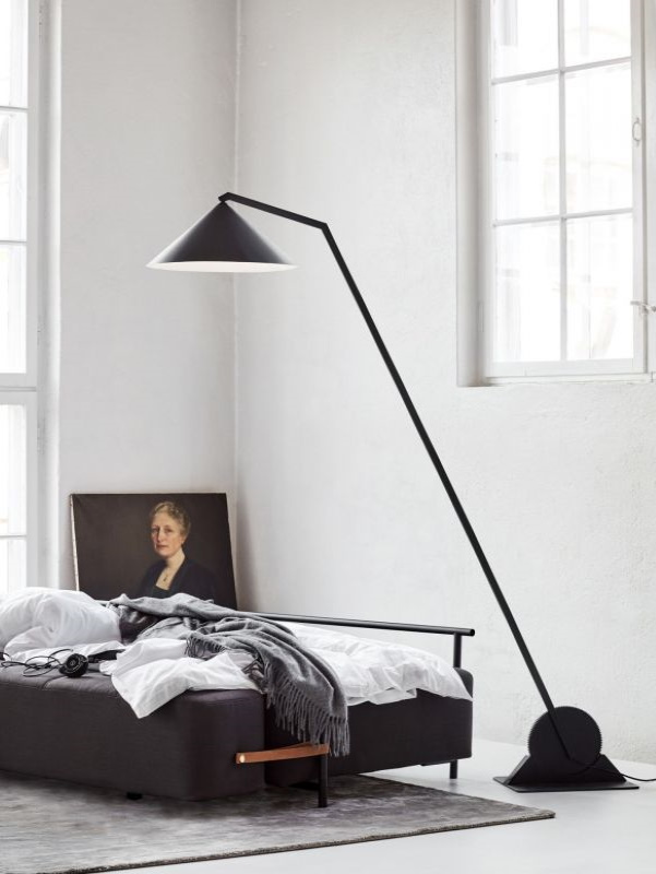Schwarze Design Stehlampe mit konischem Lampenschirm neben einem grauen Sofa in einem hellen Raum.
