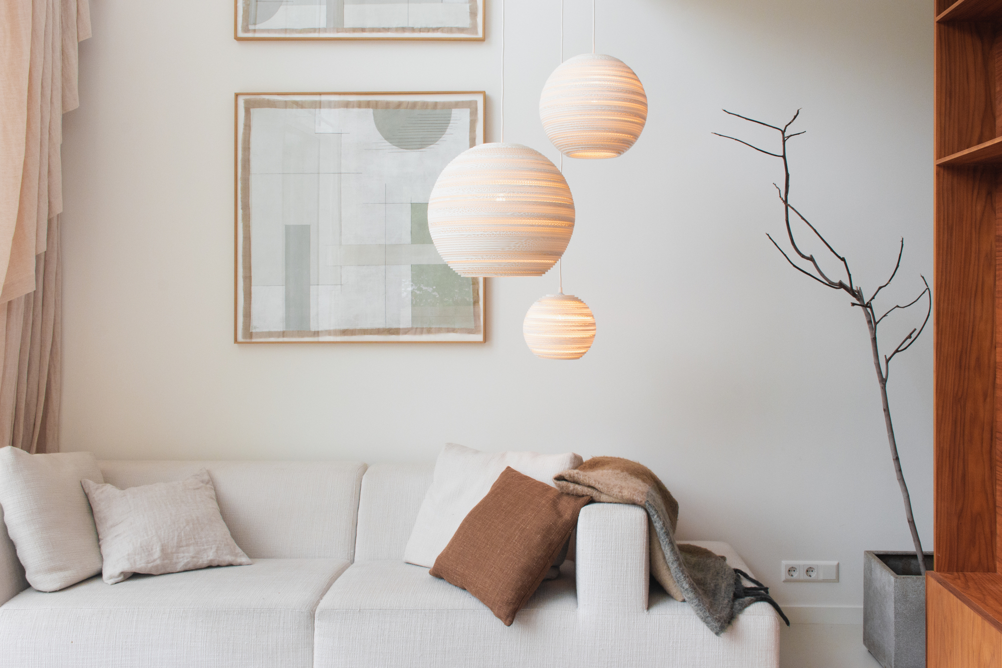 Graypants Scraplights Moon Hängeleuchten in verschiedenen Größen über einem weißen Sofa im Wohnzimmer.
