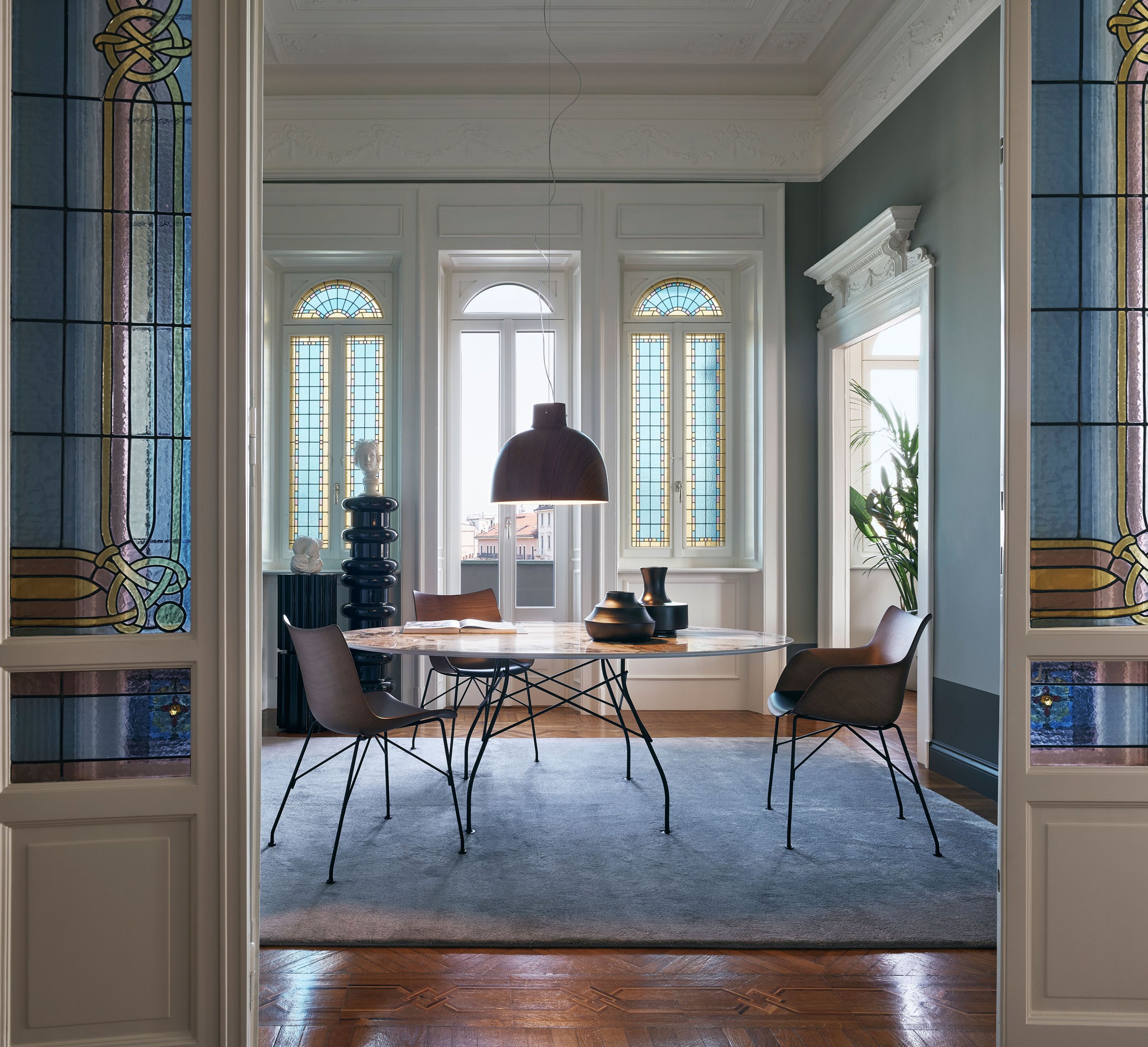 Ein runder Kartell Tisch mit marmorierter Steinzeugplatte und schwarzen Beinen in einem eleganten Esszimmer.