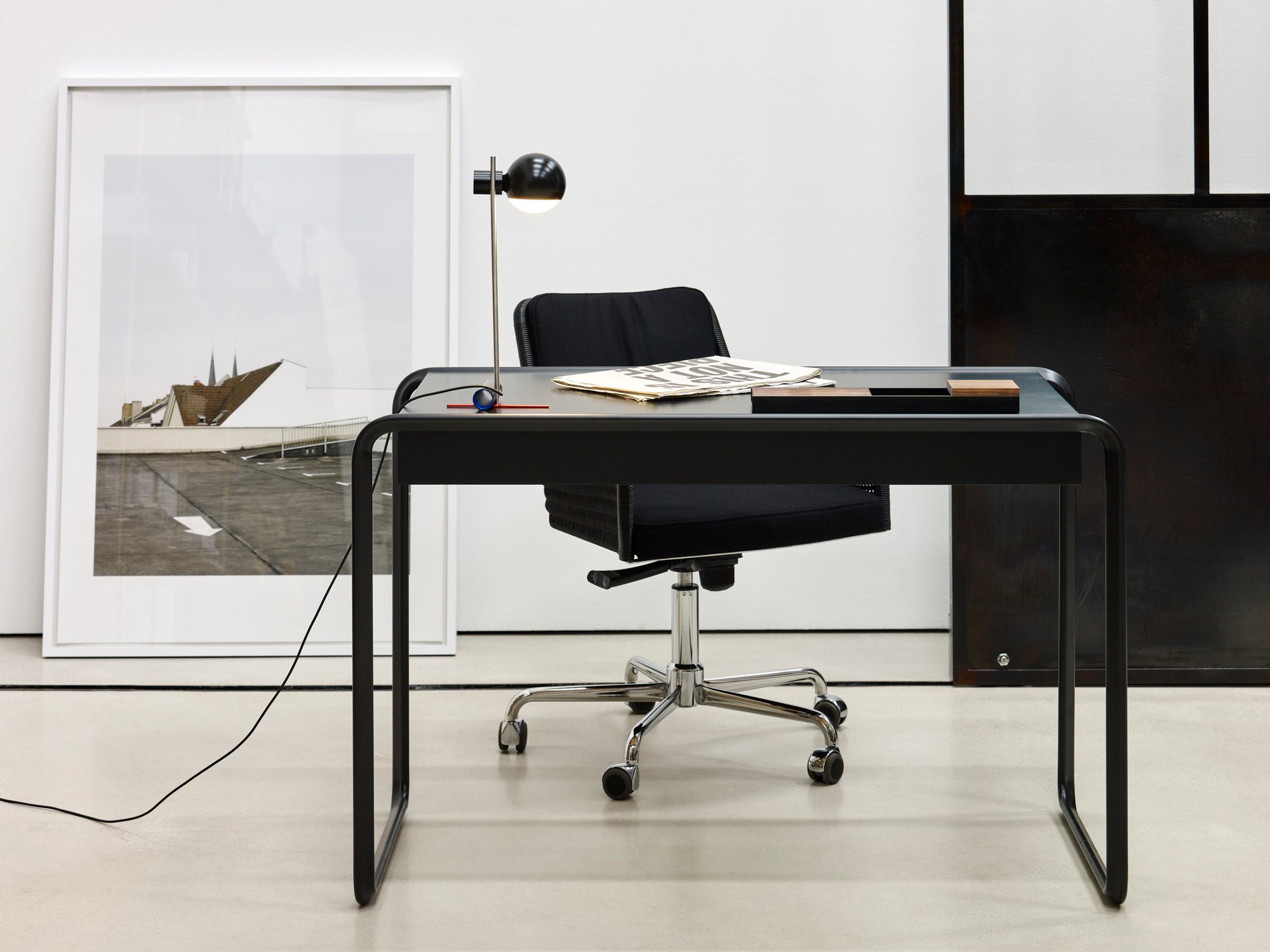 L25 Tischleuchte von Tecta auf schwarzem Schreibtisch mit Bürostuhl und minimalistischer Dekoration im modernen Büro.