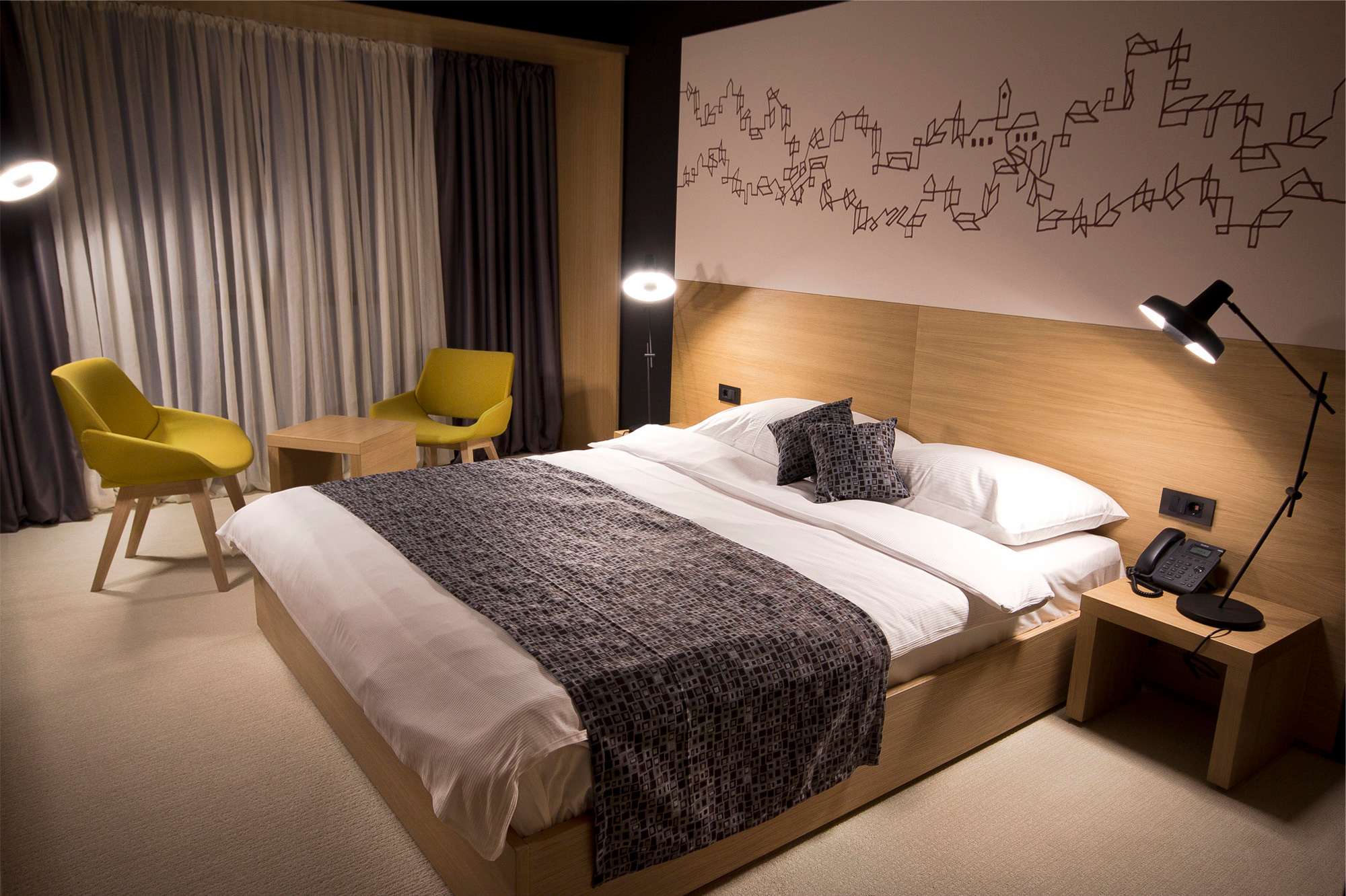 Schlafzimmer mit Doppelbett, zwei gelben Stühlen und einer Arigato Tischleuchte von Grupa, die warmes Licht spendet.