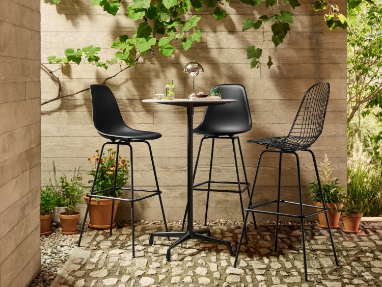 Drei schwarze Barhocker von Vitra, darunter ein Eames Wire Bar Stool, an einem Bistrotisch im Freien.