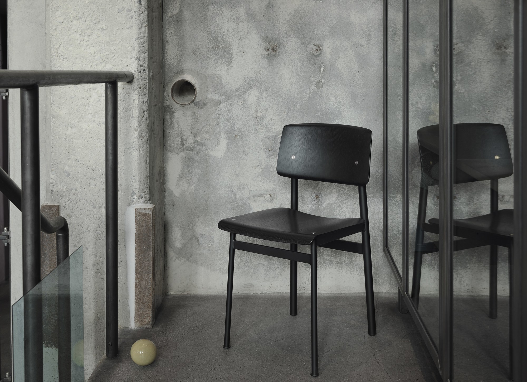 Schwarzer Loft Chair Stuhl von Muuto vor einer grauen Betonwand und Treppe.