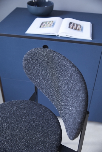 Detailaufnahme des Verpan Series 430 Barhockers mit grauem Stoffbezug und schwarzem Gestell vor blauem Sideboard.