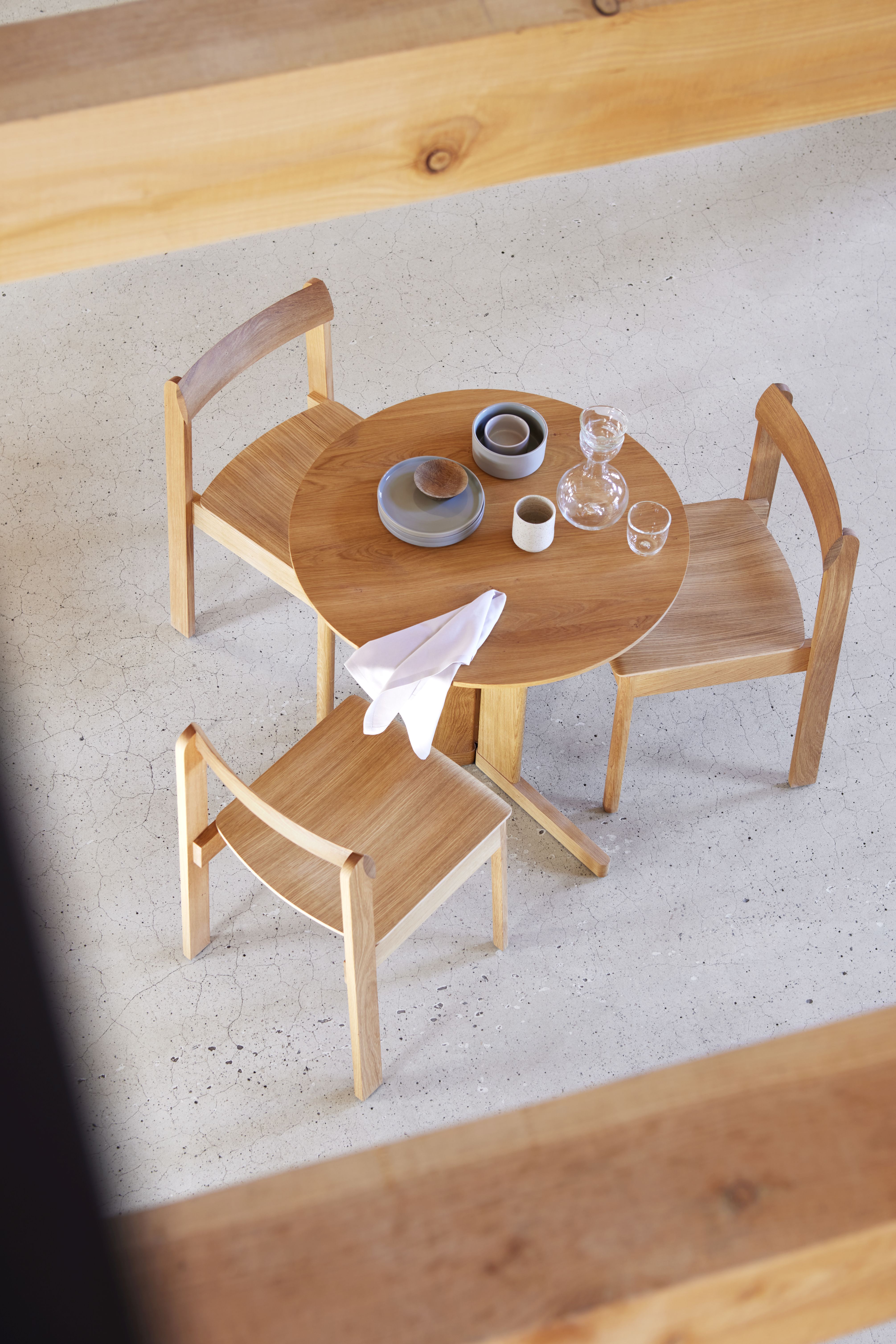 Trefoil Tisch von Form & Refine aus Eiche mit drei Stühlen und Geschirr.