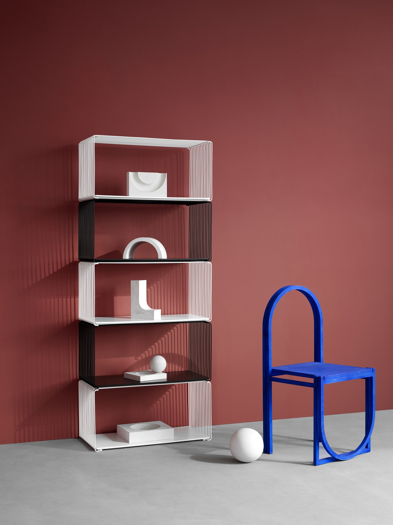 Panton Wire Regalsystem in Weiß und Schwarz mit Deko-Elementen, daneben ein blauer Stuhl.