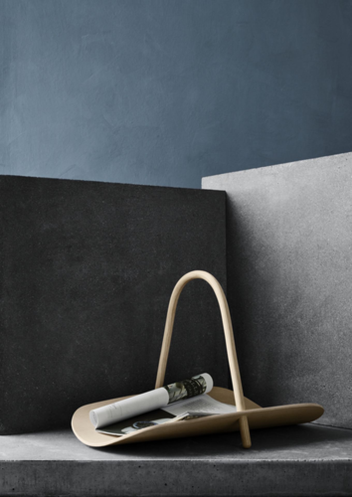 Beige Magazinablage aus Holz mit Griff und gerollter Zeitschrift vor dunklem Hintergrund.