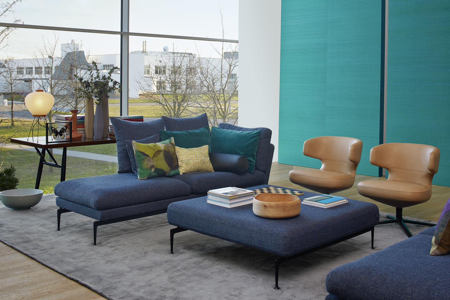 Wohnzimmer mit blauem Sofa, Ottomanen und zwei Sesseln vom Typ Vitra Petit Repos in Leder.