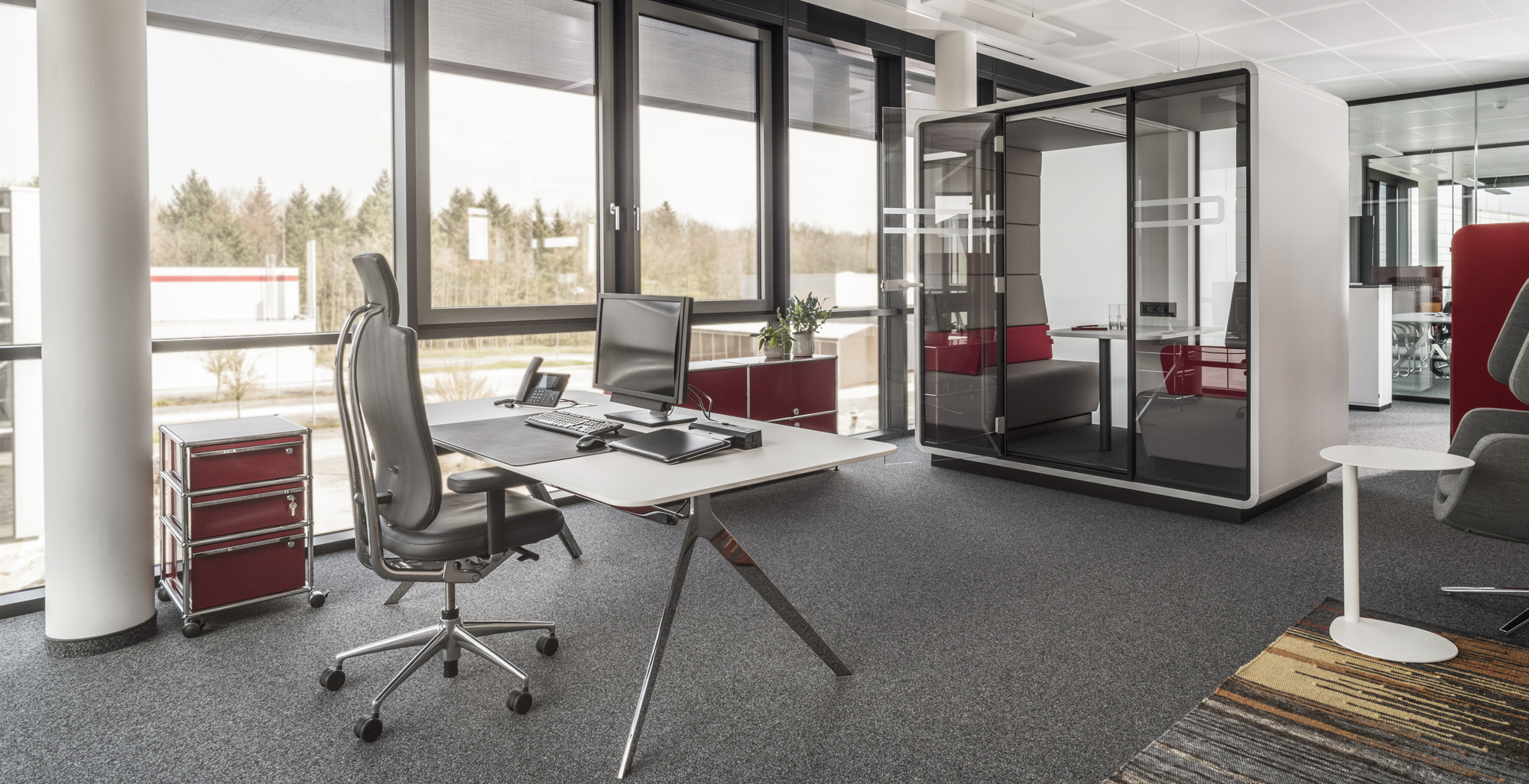 Modernes Büro mit Schreibtisch, Bürostuhl, Rollcontainer und Telefonzelle für konzentriertes Arbeiten.