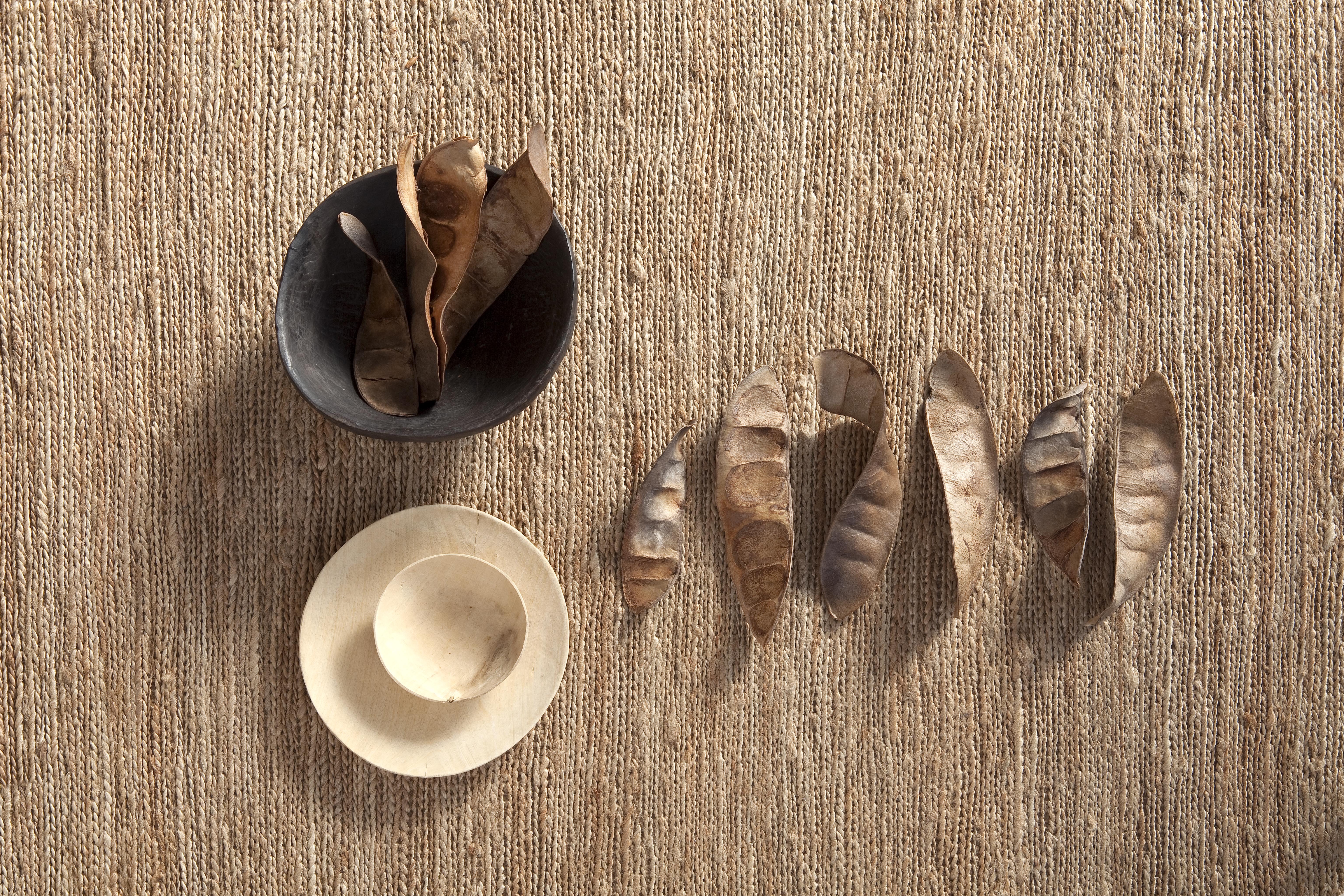 Detailaufnahme des Nanimarquina Knitted Rug Teppichs: Beige Textur mit Schalen und Samenkapseln.