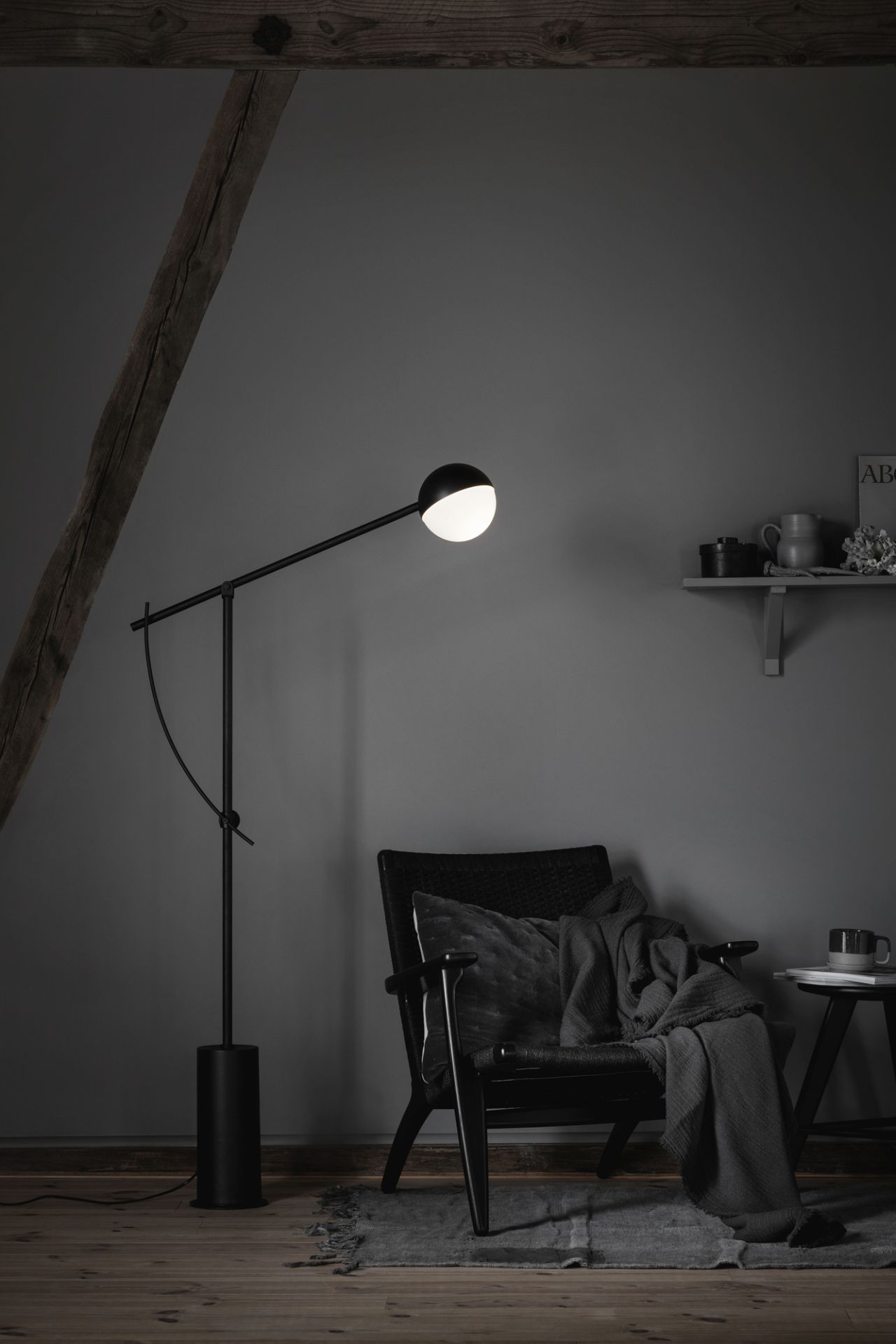 Schwarze Stehlampe mit kugelförmigem Lampenschirm neben Sessel mit Decke und Kissen in grauem Wohnzimmer.