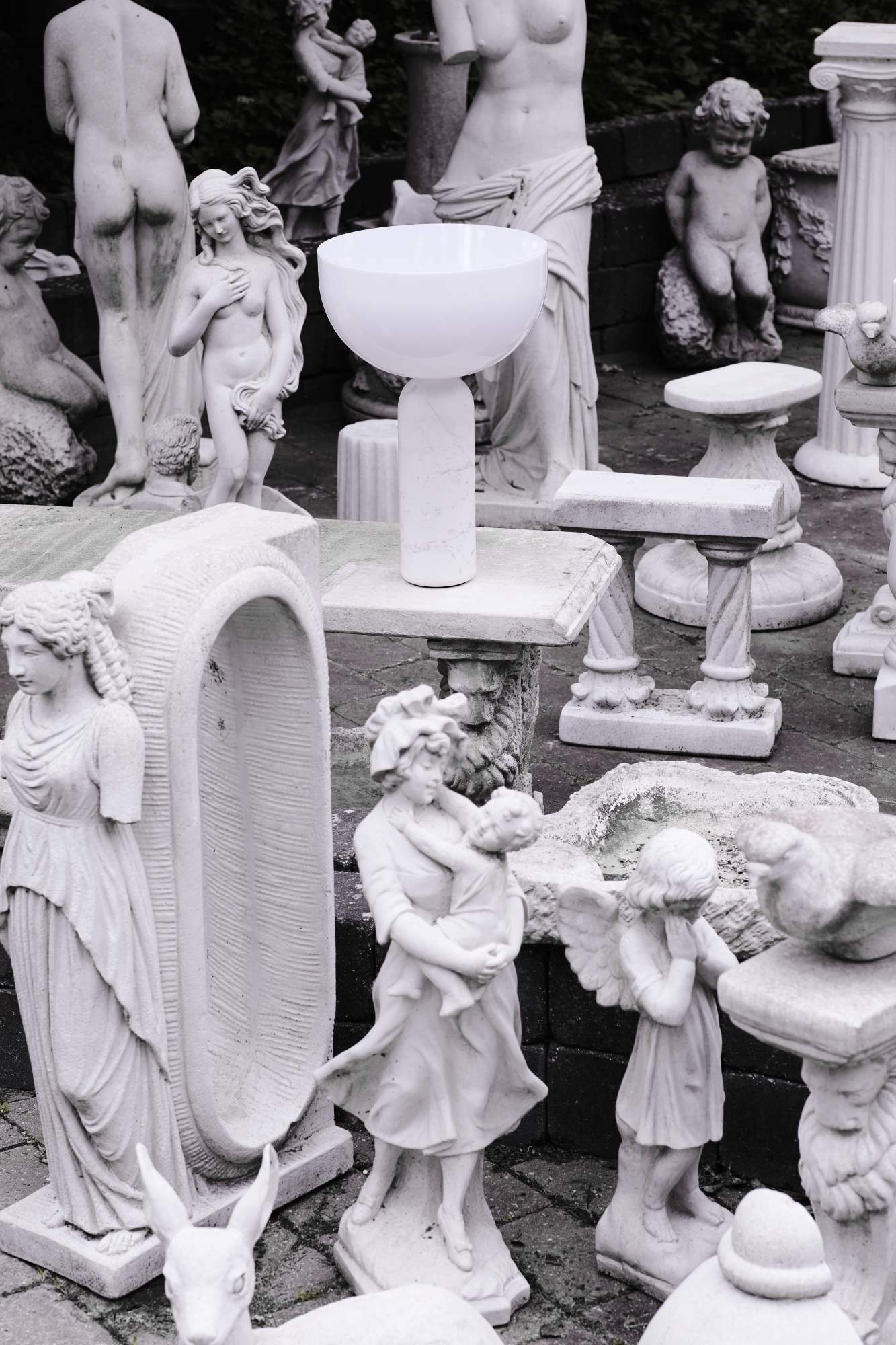 Weiße Kizu Tischleuchte von New Works zwischen Statuen. Design Lampe für Wohnzimmer und Schlafzimmer.