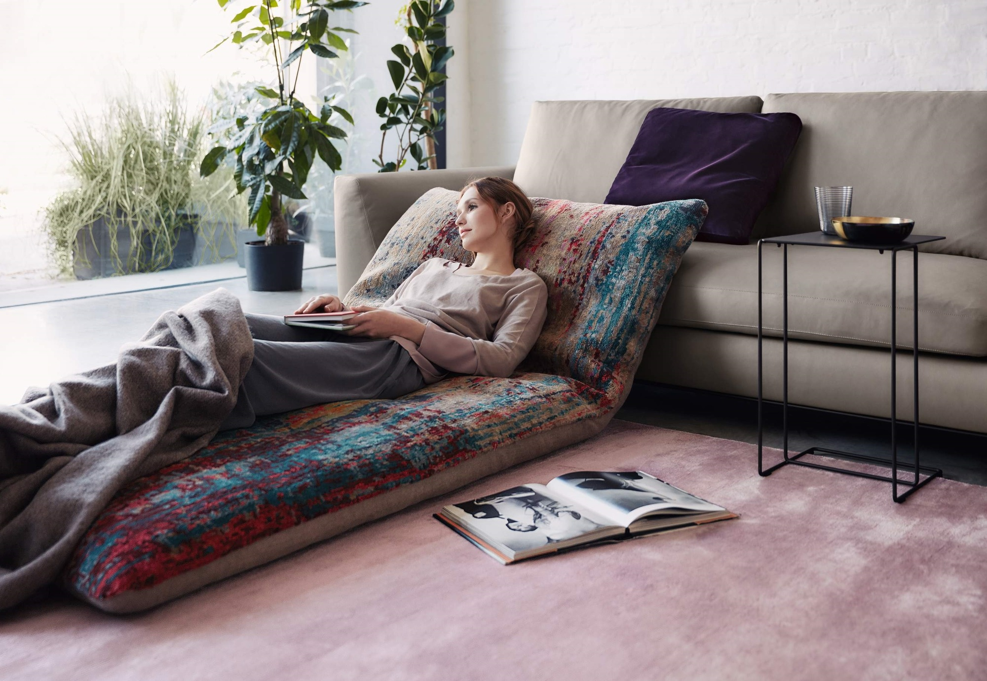 Frau entspannt auf Sofa neben Walter Knoll Beistelltisch mit Getränken, Buch und Zimmerpflanzen im Wohnzimmer.