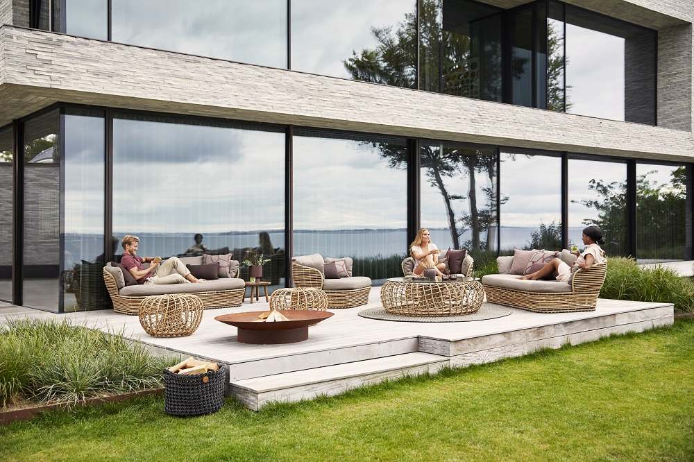 Cane-Line Basket Outdoor Sofa mit zwei Sitzen und passenden Möbeln auf einer Gartenterrasse.