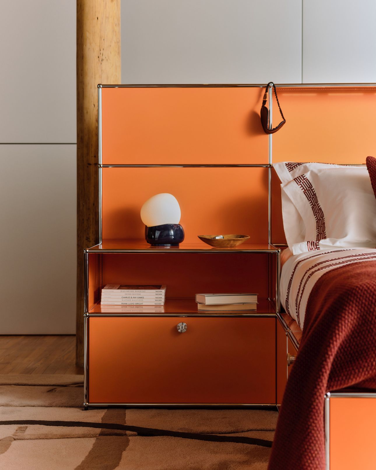Detailaufnahme des orangefarbenen USM Haller Betts von Armando Cabral mit Nachttisch und Textilien.