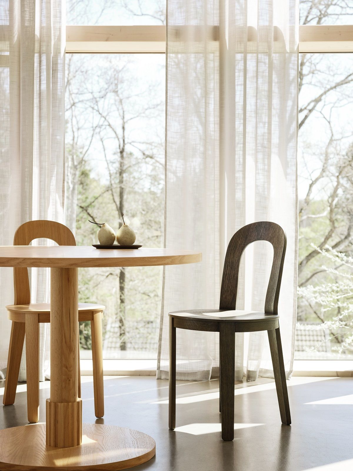 Zwei Olivia Stühle von Design House Stockholm an einem runden Holztisch vor Fenster.