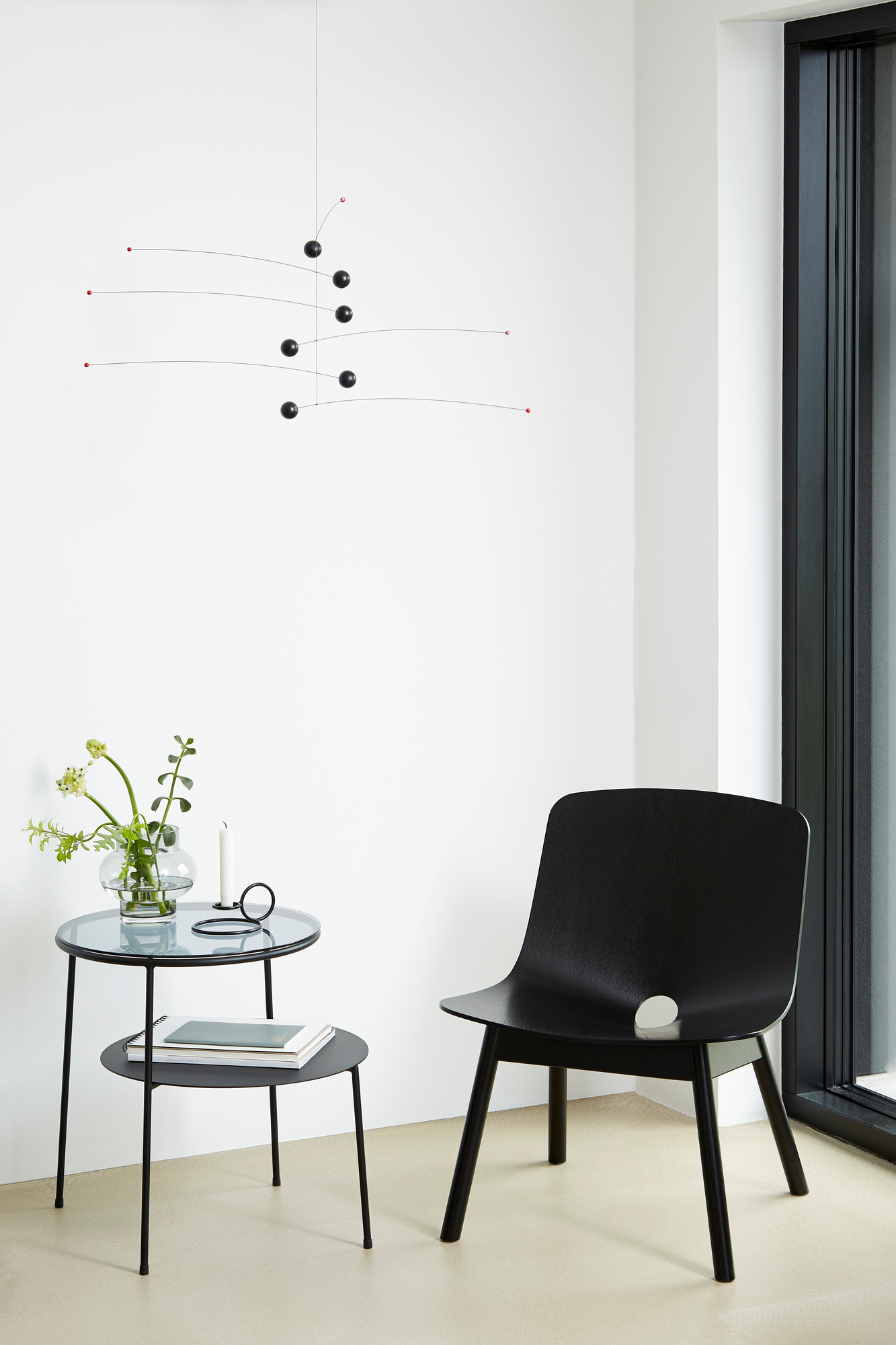 Duo Beistelltisch Schwarz mit Rauchglas von Woud, mit Dekoration und schwarzem Stuhl in minimalistischem Ambiente.