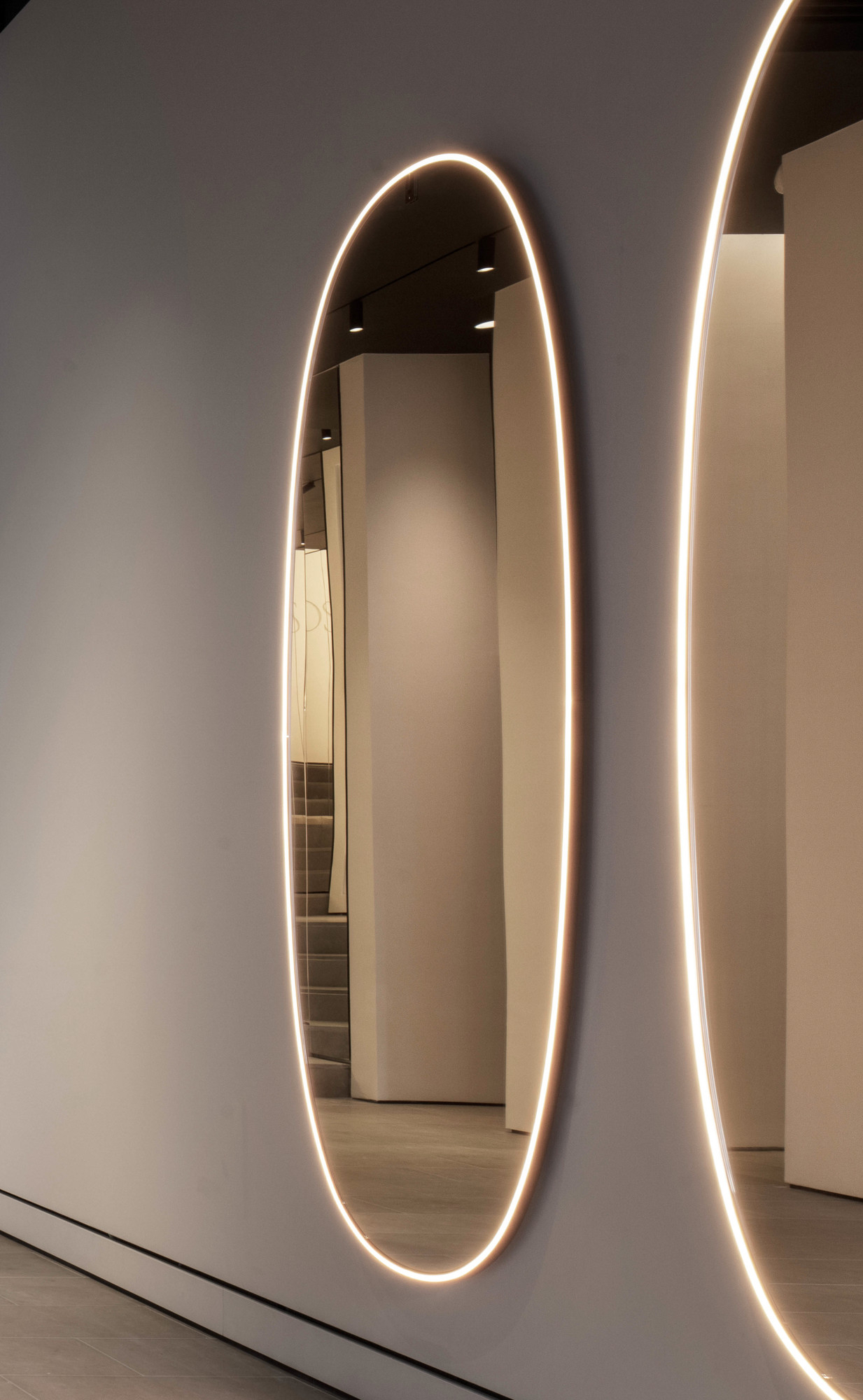 La Plus Belle Lichtspiegel von Flos an grauer Wand, ovales Design mit integrierter LED-Beleuchtung.