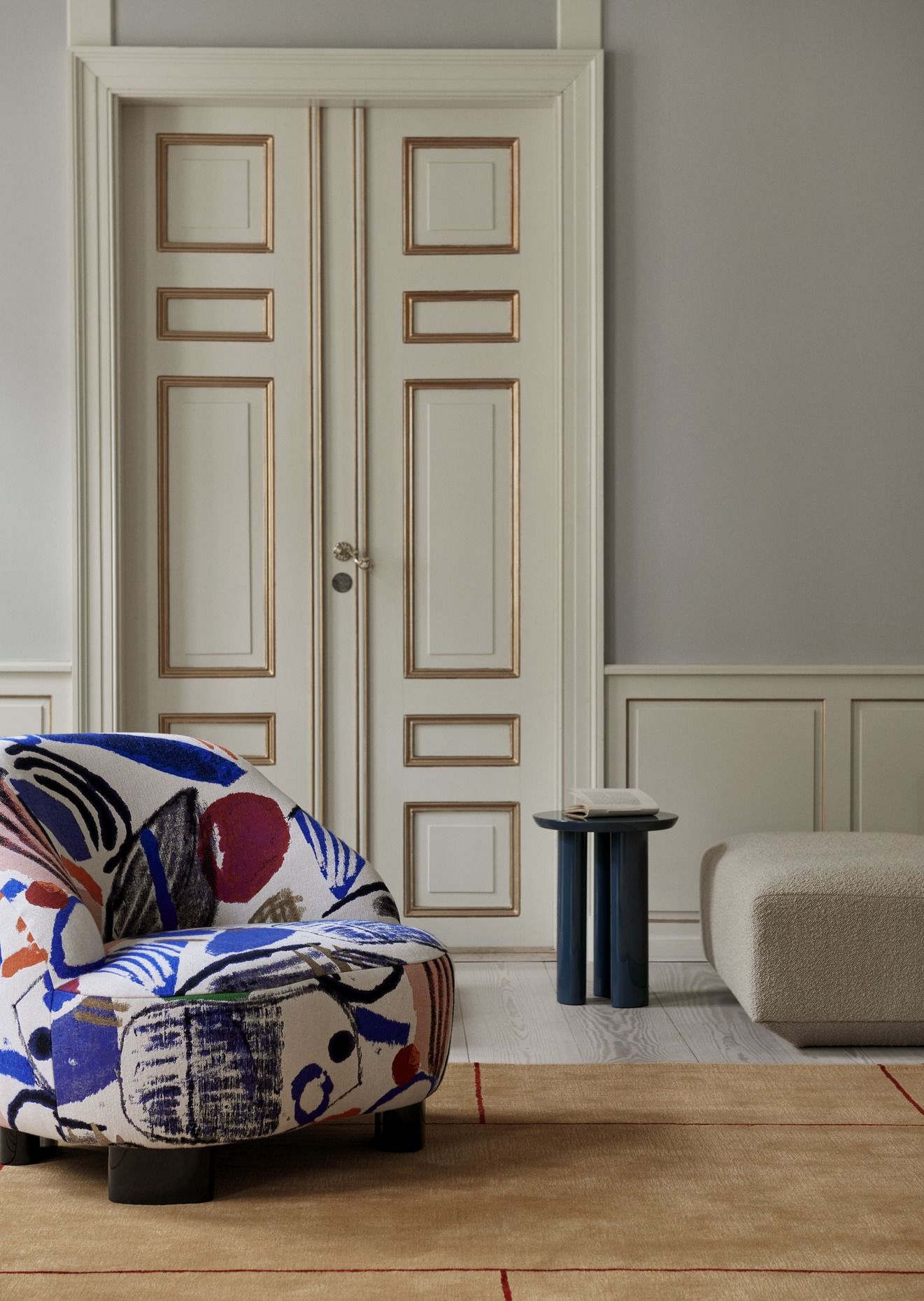 AndTradition Cruise Teppich AP11 in Beige mit rotem Muster, kombiniert mit Sessel und Beistelltisch.