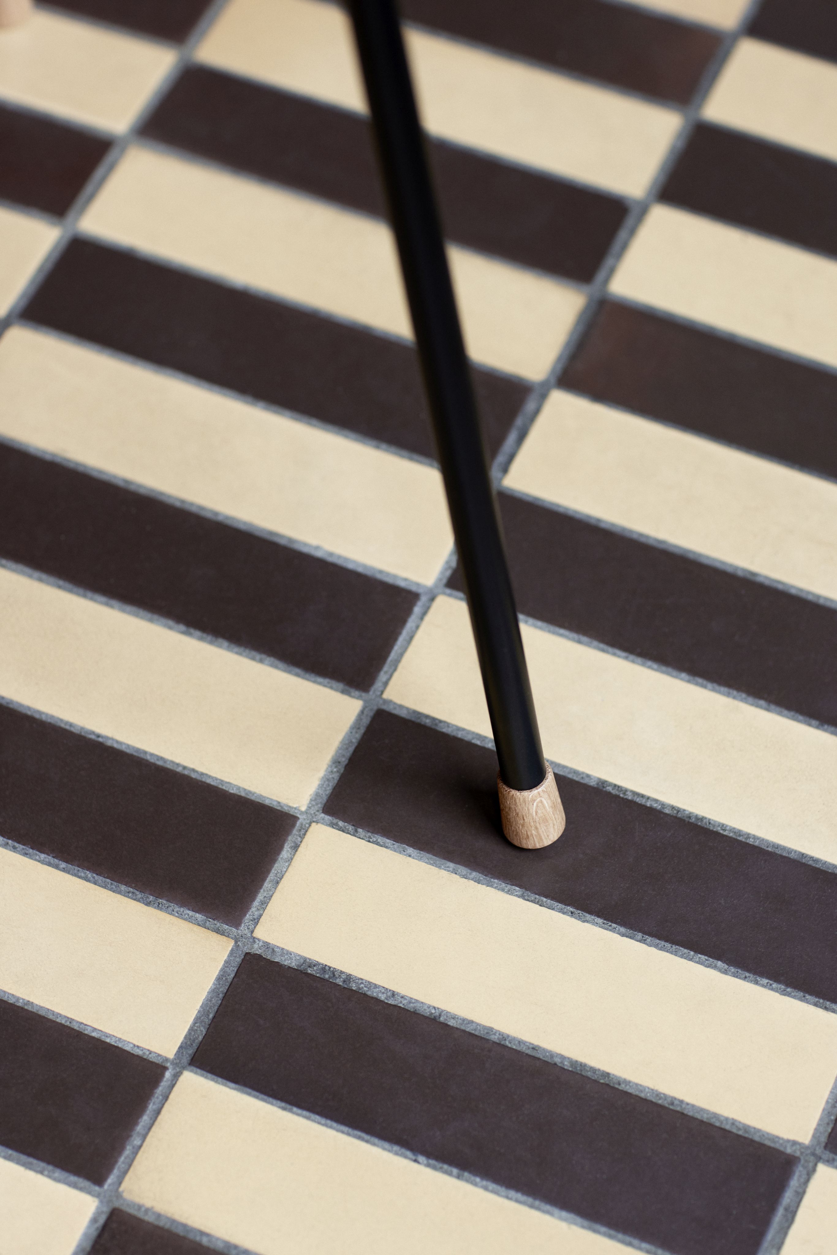 Detailaufnahme vom Bein des Carl Hansen Vega Stuhls auf einem Schachbrettmuster-Fliesenboden.