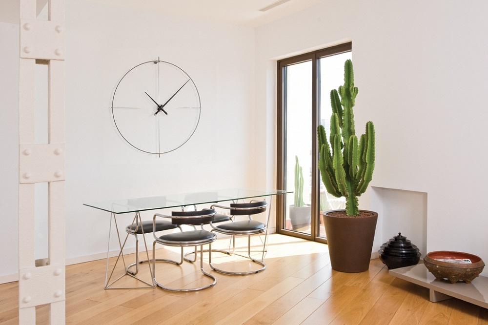 Weiße Bilbao Wanduhr von Nomon im minimalistischen Esszimmer mit Glastisch und Kaktus.