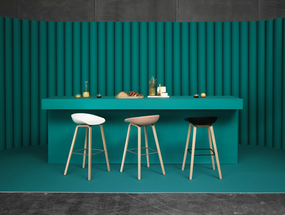Drei Hay About a Stool AAS32 Barhocker in Weiß, Beige und Schwarz vor türkisfarbenem Hintergrund.