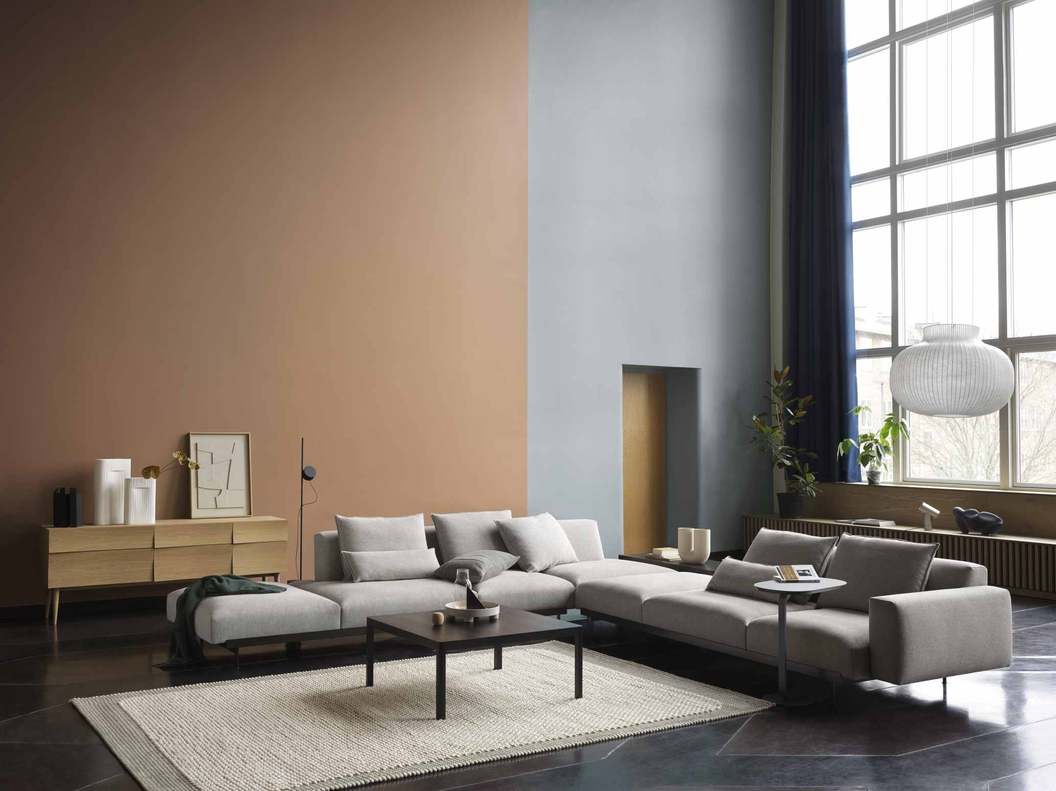 Helle Muuto Strand Pendelleuchte über modernem Wohnzimmer mit großem Fenster und grauer Couch.