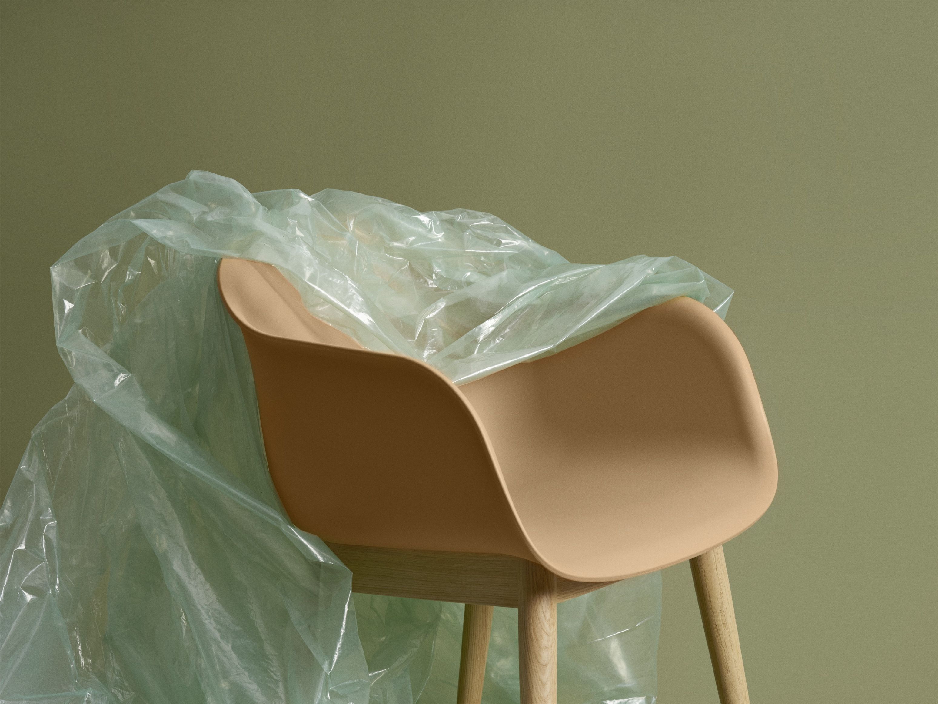 Muuto Fiber Armchair mit Holzbeinen, teilweise mit transparenter Schutzfolie bedeckt, modernes Möbeldesign für Esszimmer und Wohnbereich.