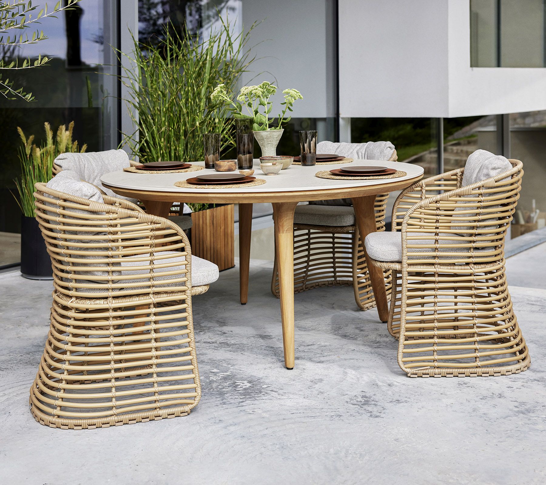 Bild eines Cane-Line Basket Sessels aus Rattan mit Esstisch und Stühlen im Außenbereich.