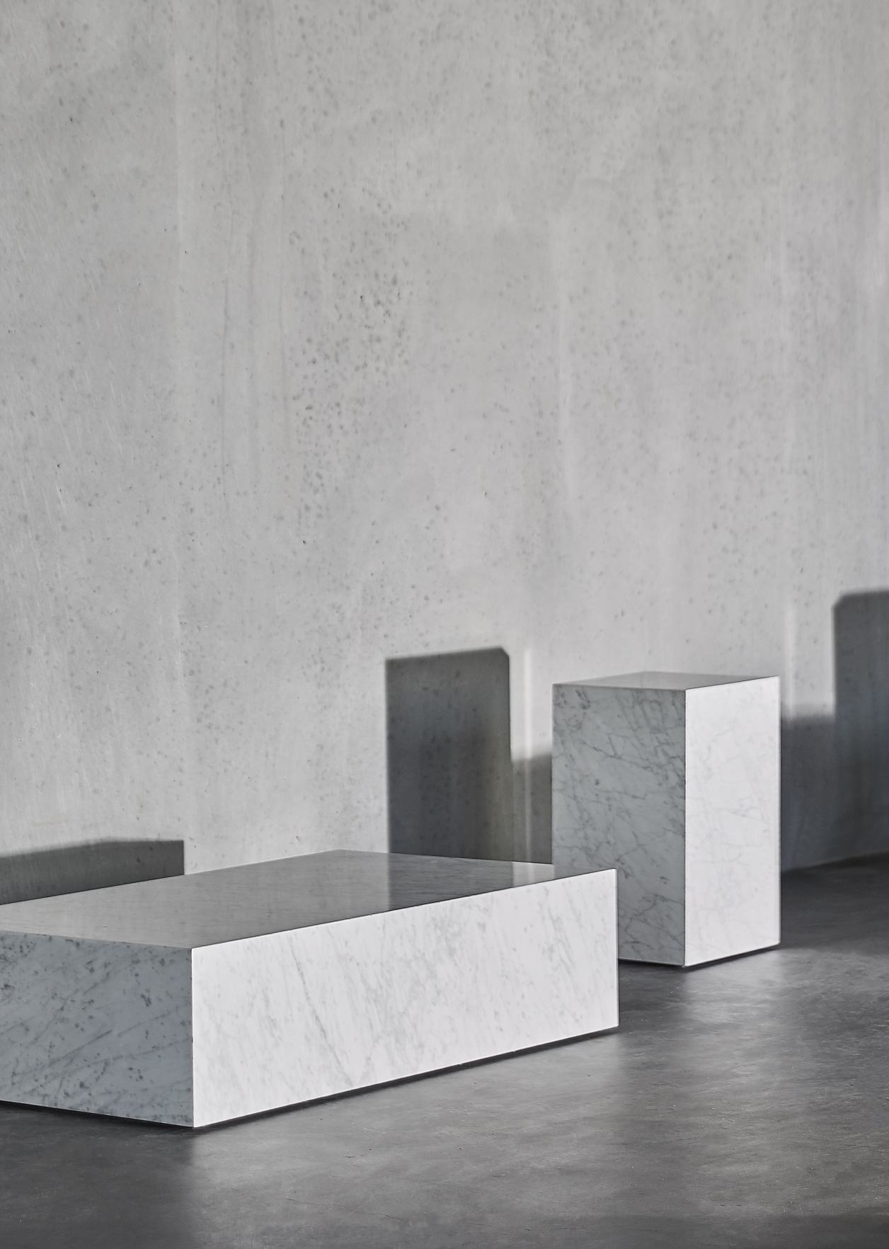 Audo Plinth Cubic Beistelltisch aus Marmor, rechteckig und quadratisch, vor grauer Wand.