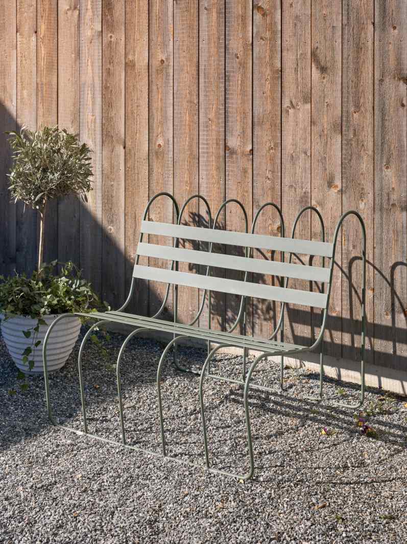 Gardener's Sofa von Design House Stockholm: Grüne Gartenbank aus Metall vor Holzwand und Pflanze.