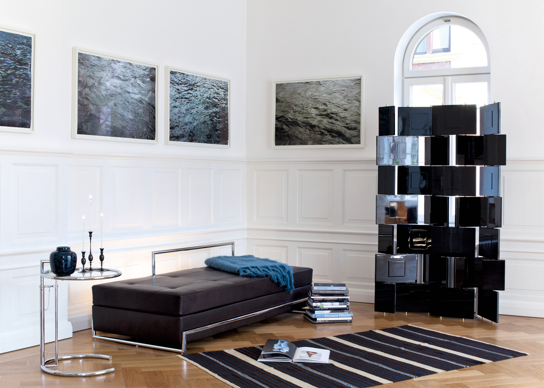 Adjustable Table E1027 Beistelltisch von ClassiCon neben einer modernen Ottomane in einem stilvollen Wohnzimmer.