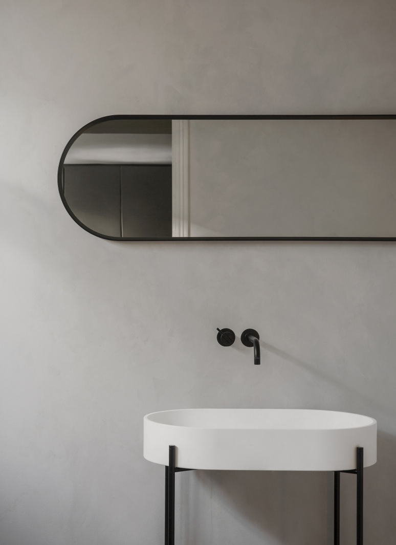 Norm Wall Mirror Oval von Audo: Ovaler Wandspiegel mit schwarzem Rahmen über einem weißen Waschbecken.