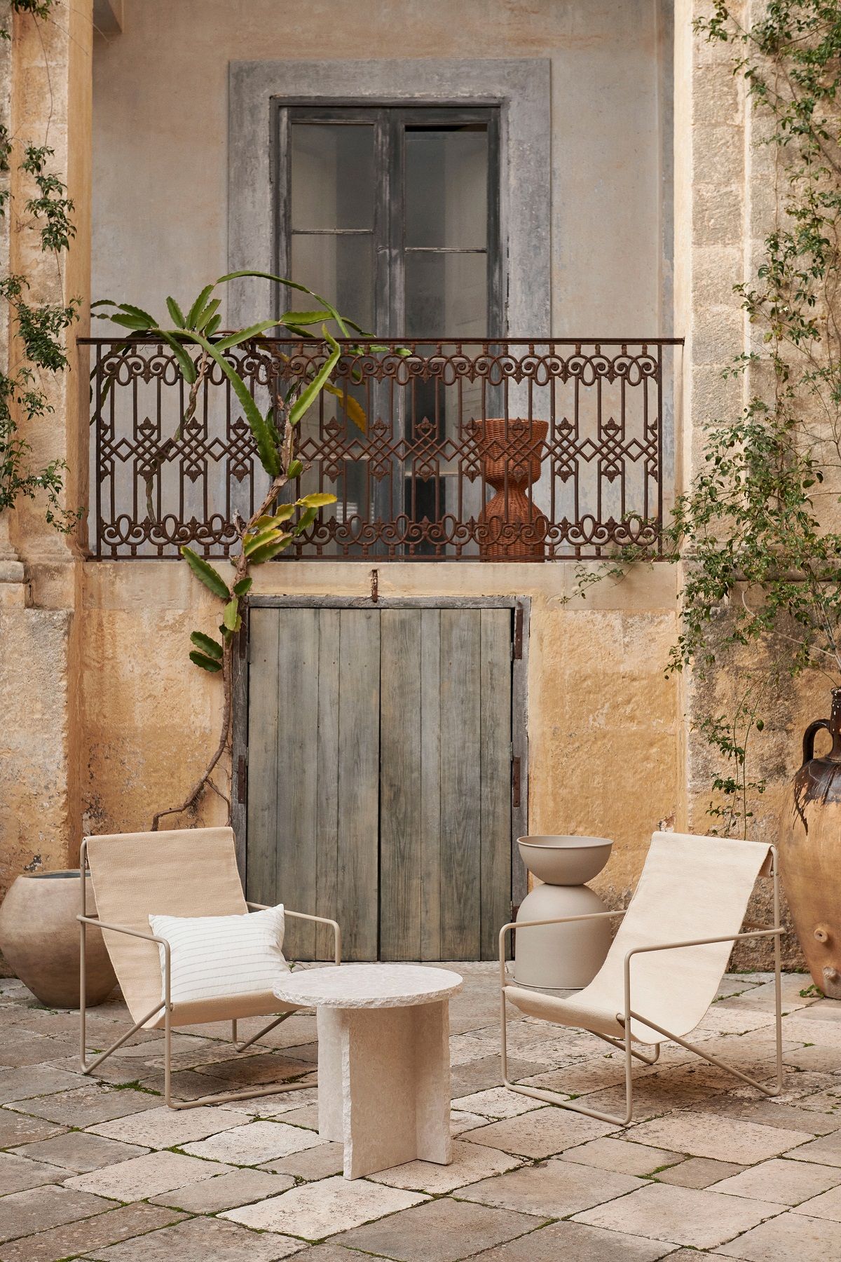 Ferm Living Desert Chair Loungesessel in Beige mit Beistelltisch und Kissen im mediterranen Außenbereich.