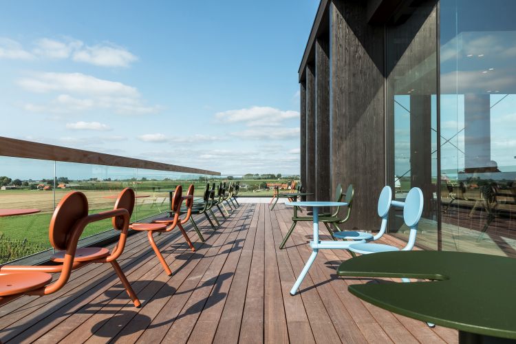 Extremis Bistroo Stühle und Tische in verschiedenen Farben auf einer Holzterrasse mit Ausblick.