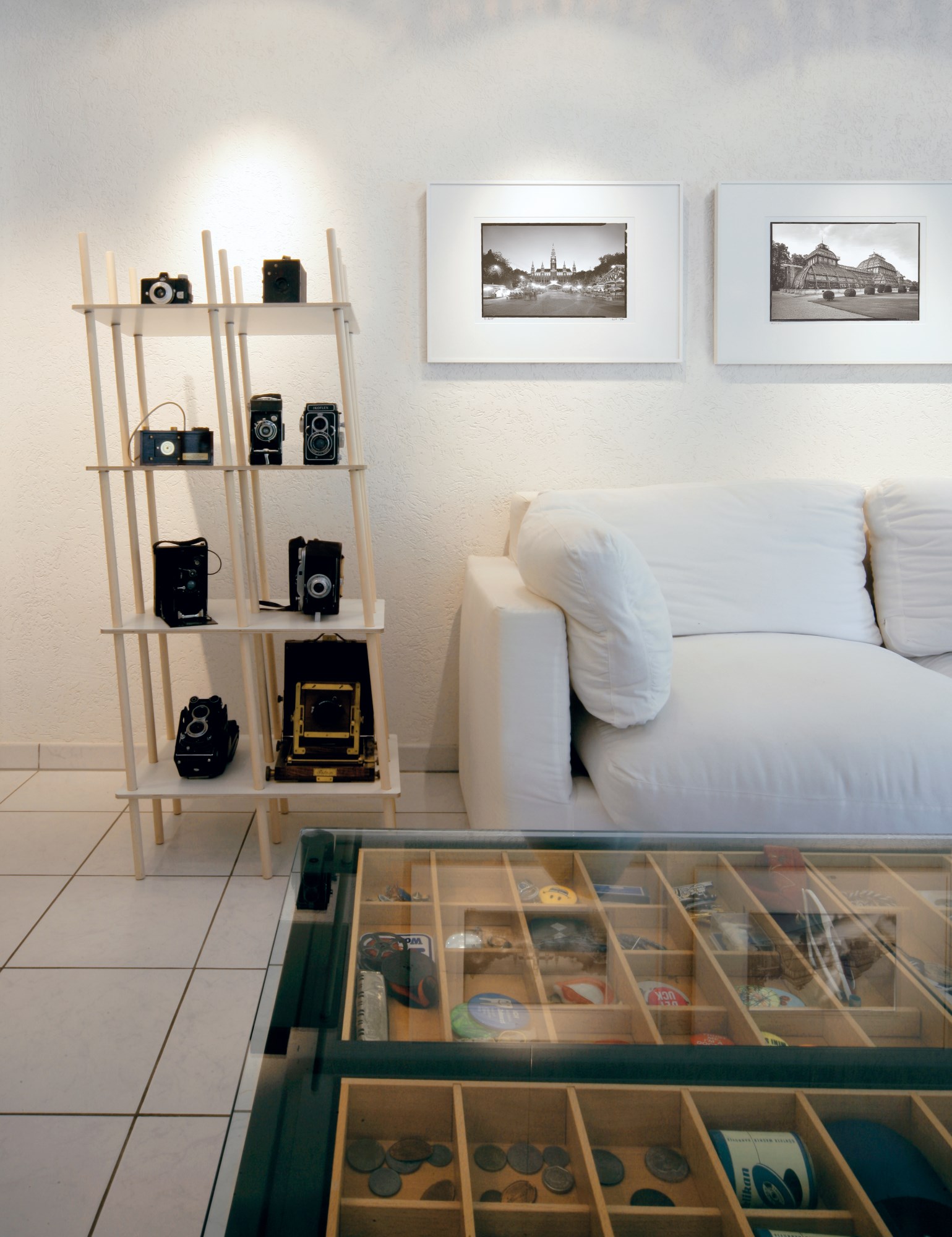 Helles Regal "Nils" von Moormann mit alten Kameras vor weißer Wand und Sofa im Wohnzimmer.