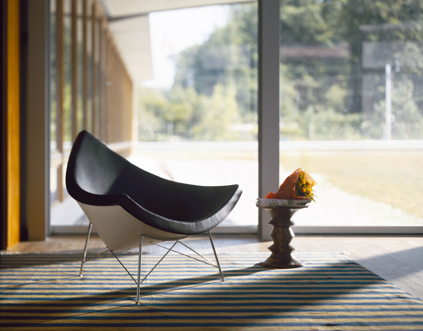 Schwarzer Coconut Chair von Vitra auf einem gestreiften Teppich vor einem Fenster mit Blumenstrauß.