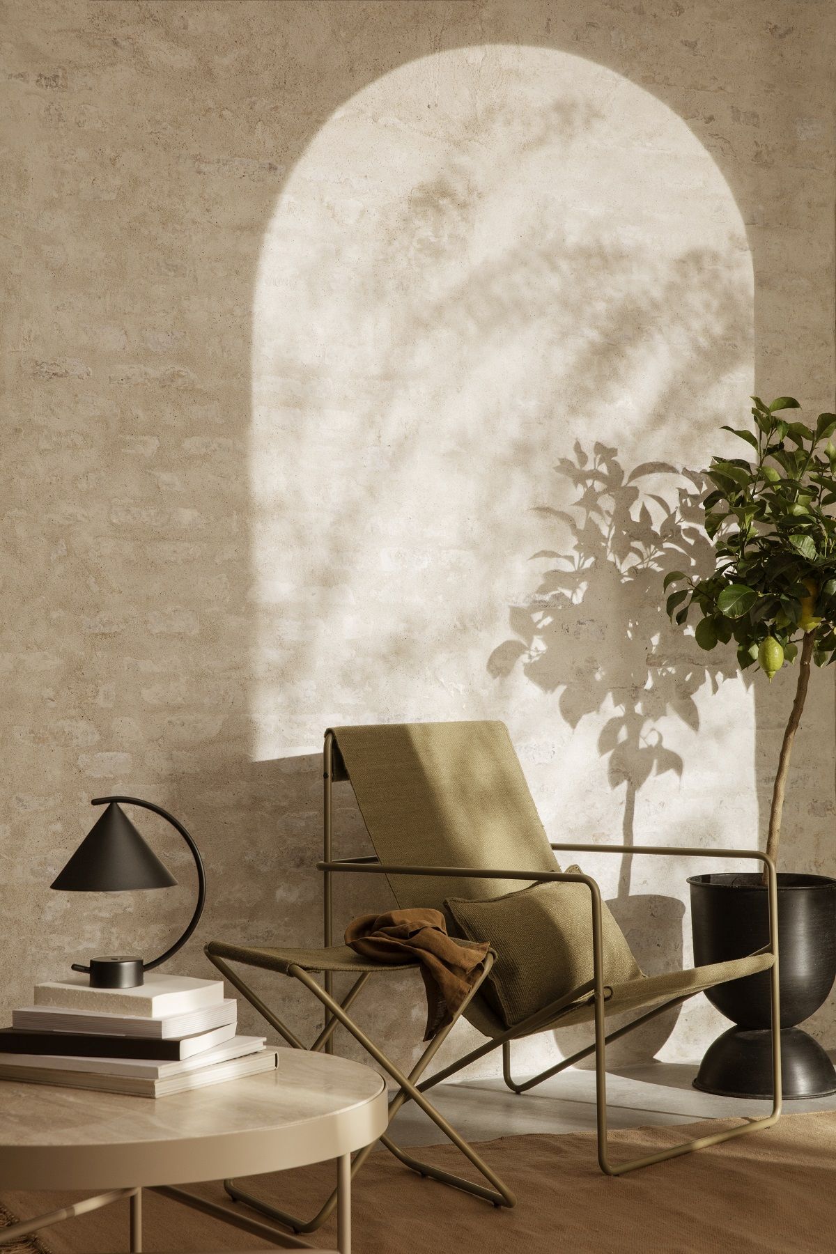 Desert Chair Loungesessel von Ferm Living in Khaki mit Beistelltisch, Lampe und Pflanze.