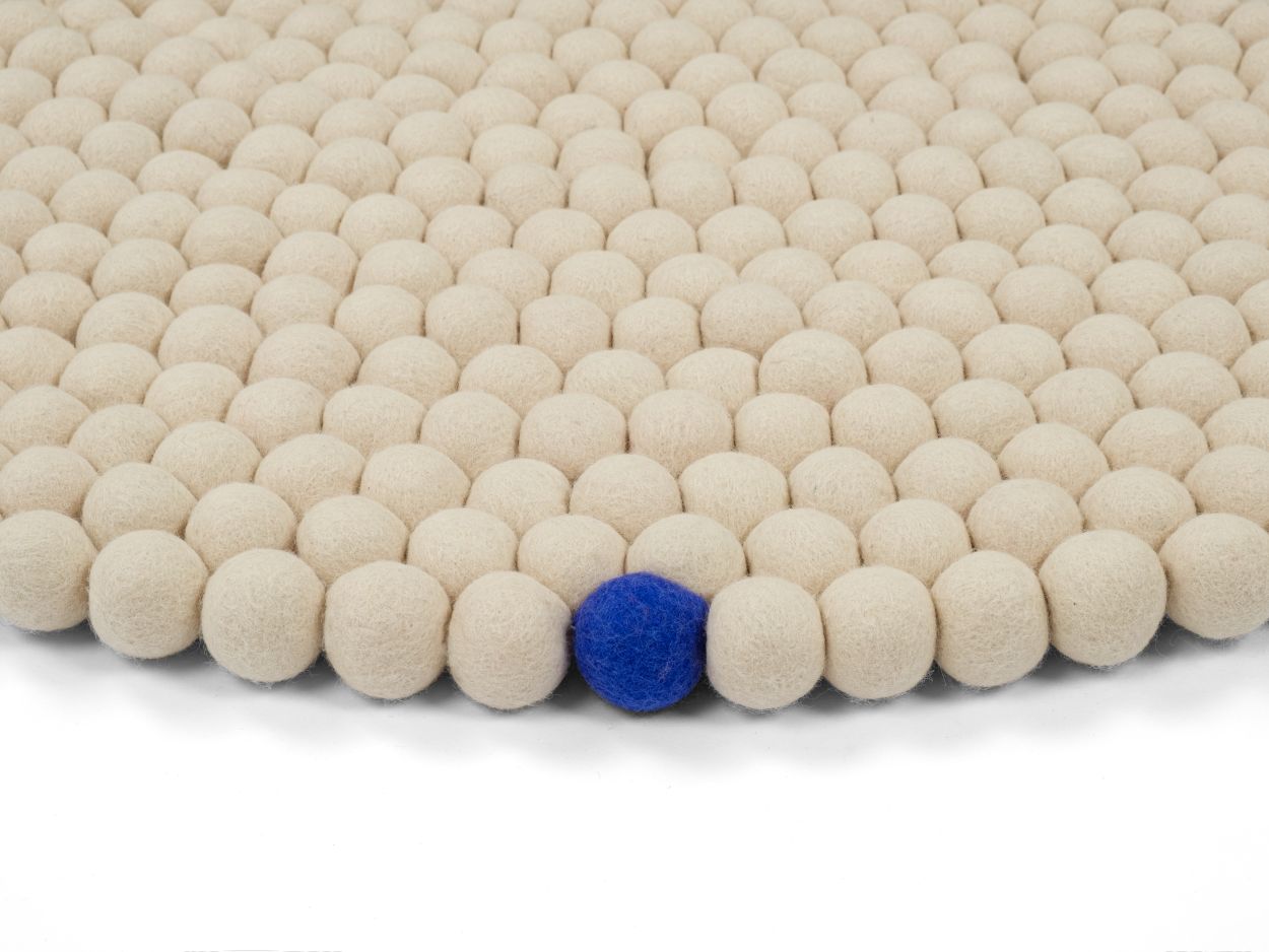 Detailaufnahme des runden myfelt Filzteppichs "Big One" in Creme mit einer blauen Filzkugel.