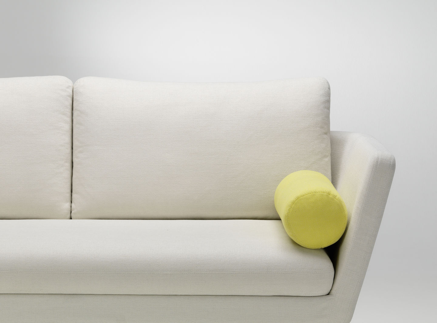 Nahaufnahme eines weißen Sofas mit rechteckigen Kissen und einem gelben, zylinderförmigen Vitra Kissen.
