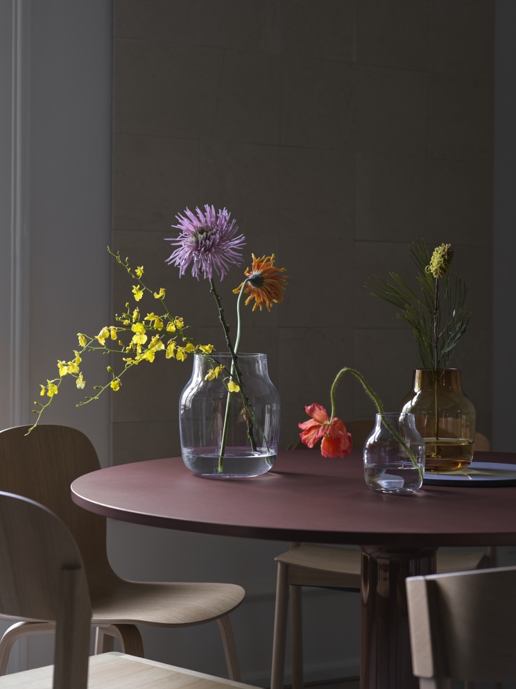 Nahaufnahme des runden Muuto MIDST Table Esstisch mit Blumenvasen und Stühlen in gedämpftem Licht.