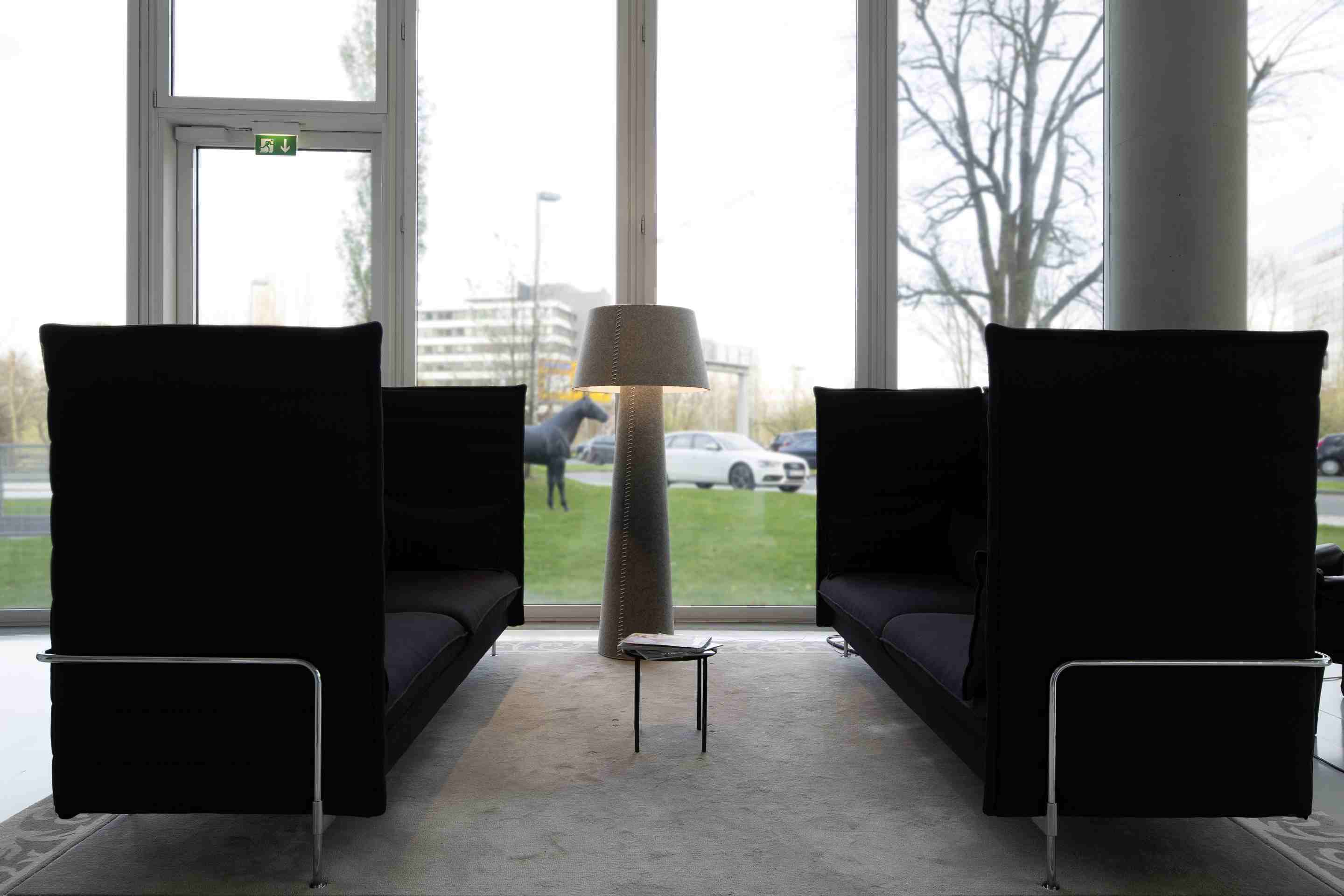 Moree Alice XL Stehleuchte im modernen Büro-Lounge-Bereich mit schwarzen Sofas und Fensterfront.